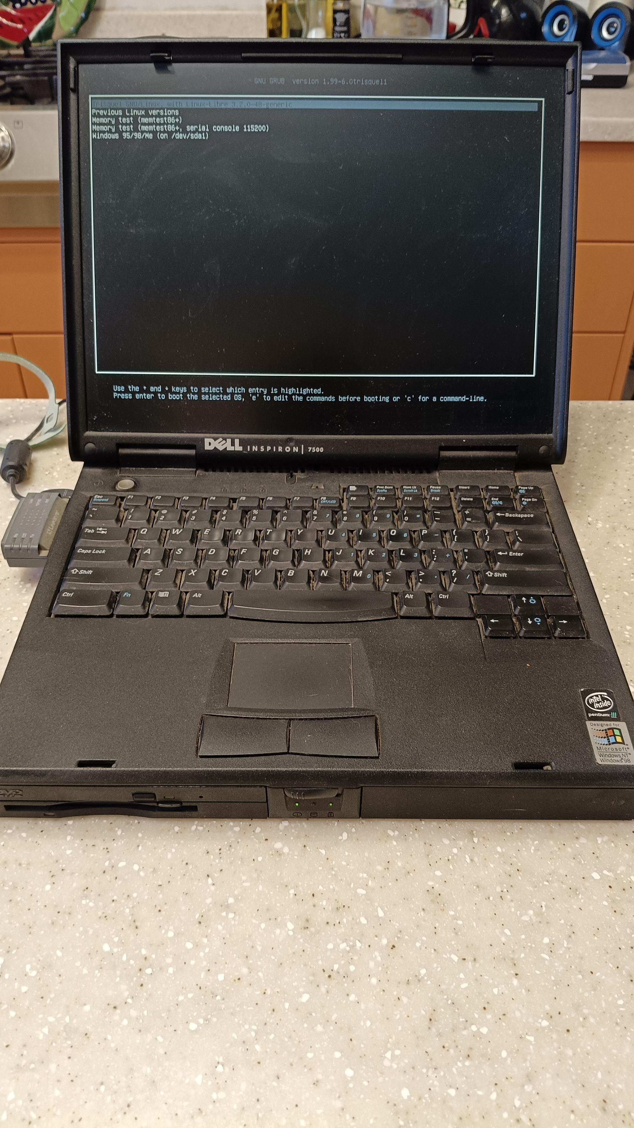 Old Dell laptop on kitchen counter booting up. Laptop is black and chunky 

Screen is open and you can see the boot loader preferences asking for which system to boot. 

Computer freezes at this point