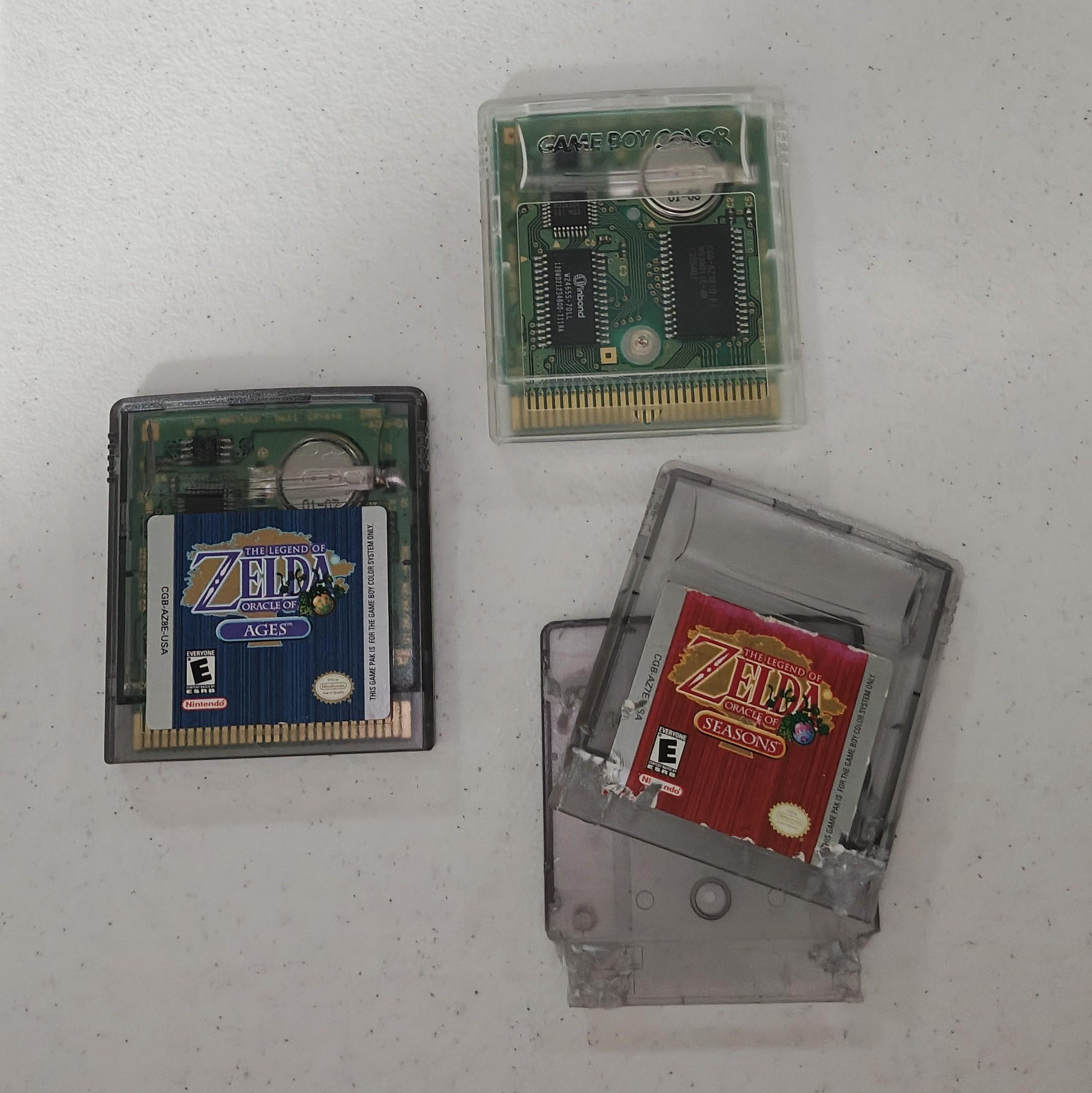 A copy of Legend of Zelda: Oracle of Ages on a table beside a chewed-up shell for Oracle of Seasons. Above it is a blank cartridge with the insides of Oracle of Seasons transferred into it.